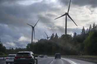 Tourist traffic on the A9 motorway during thunderstorms, wind turbines in the pine forest in the