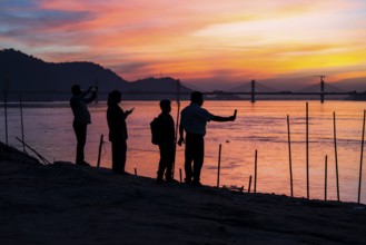 People enjoy the vibrant sunset by the Brahmaputra riverside, capturing photos and moments against
