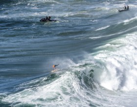 Surfers with their jet ski pilots in the Atlantic waves below Farol de Nazaré, Forte São Miguel,