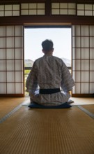 Young man wearing kimono sitting in traditional Japanese living room with tatami mats and shoji