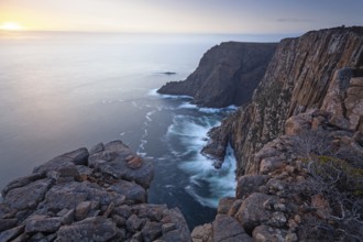 Long exposure shows sunset over the cliffs of Cape Raoul. Golden light hits the sea and colors the