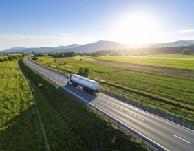 Petrol cargo truck lorry tanker driving on highway hauling oil products at sunrise, wide hilly