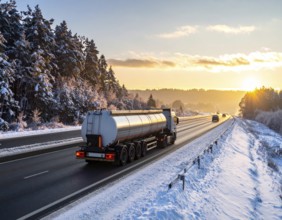 Petrol cargo truck lorry tanker driving on highway hauling oil products at sunrise, wide snowy