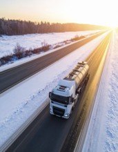 Petrol cargo truck lorry tanker driving on highway hauling oil products at sunrise, wide snowy