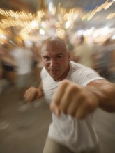 A man gets into a fighting stance, surrounded by dynamic movement and a background filled with
