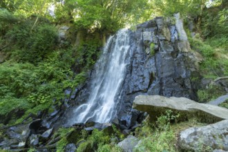 Vaucoux waterfall cascades gracefully over dark rocks, surrounded by lush greenery, Auvergne