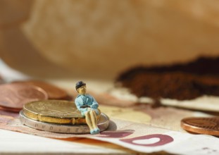 Miniature figure of a woman sitting on coins and banknotes, ground coffee in a filter bag in the