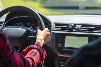 Woman driving a car, holding the steering wheel with left hand and using gps navigation on the