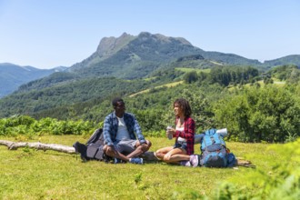 Two hikers are taking a break, sitting on grassy mountaintop and enjoying refreshing drinks with