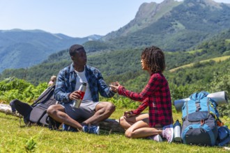 Young hikers sharing a hot drink from a thermos while resting on a mountain top during a summer