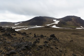 Barren volcanic landscape with snow fields, volcanic rock, mountain peaks with rain clouds,