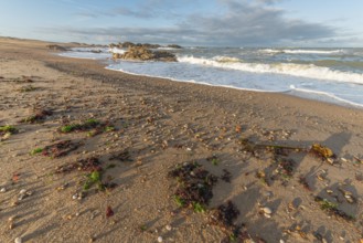 The waves crash gently against a rocky shoreline at sunset, creating a tranquil atmosphere. The