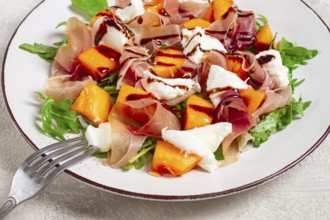 Salad with slices of ripe melon, prosciutto, mozzarella and fresh arugula, decorated with balsamic
