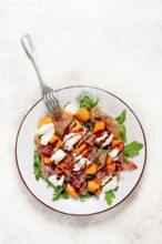 Salad with slices of ripe melon, prosciutto, mozzarella and fresh arugula, decorated with balsamic