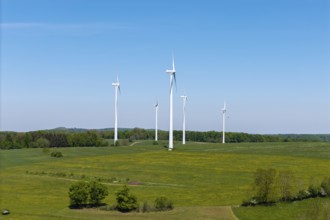 Wind turbines stand on a green area, surrounded by trees under a clear sky, Swabian Alb,