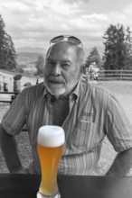 Elderly gentleman with beard and sunglasses in a garden restaurant with a drink, black and white,