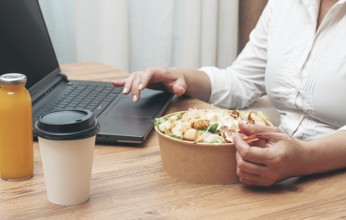 A woman is working on a laptop at home, there is food on the table, salad, coffee and juice,