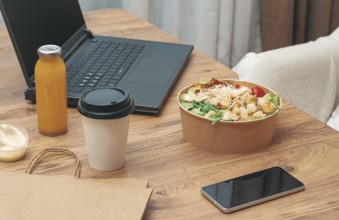 Work at home on a laptop, there is food on the table, salad, coffee and juice, delivery, there are