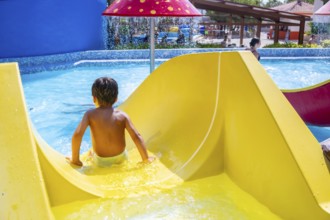 Young boy enjoying a thrilling ride down a vibrant waterslide at a lively water park, embracing the