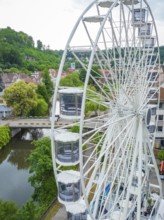 A Ferris wheel near a river, surrounded by trees and buildings, Ferris wheel construction for the