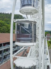 Three gondolas of a Ferris wheel, surrounded by green landscape and sky, Ferris wheel construction