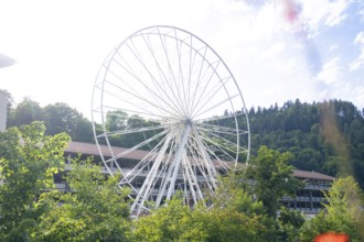 Large white Ferris wheel in front of a building and wooded hills, Ferris wheel construction for the