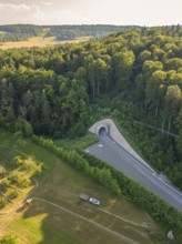 A bird's eye view of a railway tunnel in the middle of a wooded hill at sunset, construction of the
