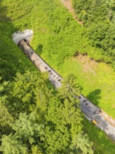 A train disappears into a tunnel, surrounded by forest in a bird's eye view, construction of the