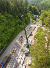 Construction site along railway tracks in a dense forest, crane in action, construction of the