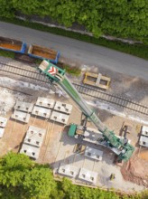 Crane on construction site on railway tracks, concrete blocks laid out next to a green forest