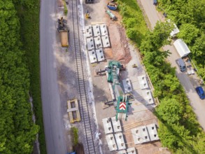 Aerial view of a construction site on railway tracks surrounded by forest with a green crane,