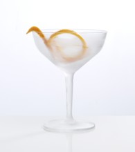 Frosted empty cocktail glass with orange zest as garnish against a white background, studio shot