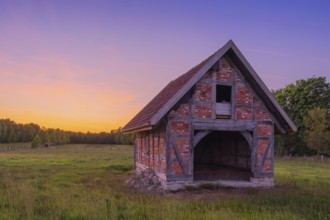 View of an open half-timbered barn standing on a pasture in the sunset, meadow, spring, awakening,