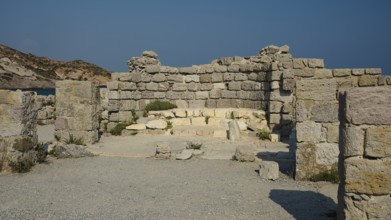 Remains of an ancient stone structure under a clear blue sky, Agios Stefanos Beach, Agios Stefanos