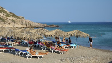 Beach scene with deckchairs and beach mats under umbrellas near the sea, Agios Stefanos Beach,