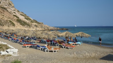Sandy beach beach with sun loungers and parasols, surrounded by rocky hills, Agios Stefanos Beach,