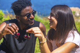 Young man and woman laughing together while sharing fresh cherries, savoring the joy of a sunny