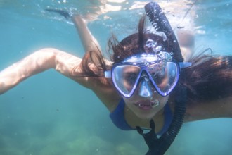 Tourist enjoys snorkeling in crystal clear ocean water, creating a stream of bubbles as she