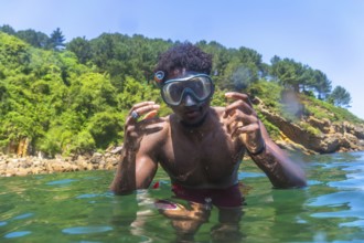 Young man wearing a snorkel mask and gesturing while swimming in green, translucent water near a