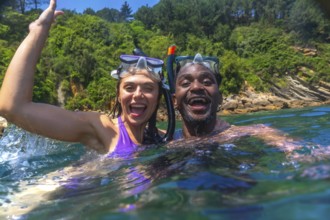 Interracial couple wearing snorkeling masks enjoys swimming in the ocean during summer vacation,