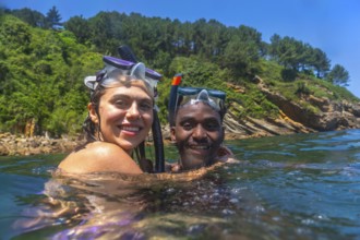 Interracial couple enjoying snorkeling adventure, embracing in refreshing ocean waters with scenic