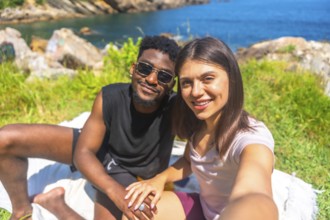 Young multiracial couple holding hands and taking a selfie while enjoying a sunny day by the sea
