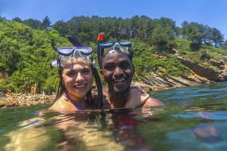 Interracial couple snorkeling in the clear blue sea, surrounded by a stunning green cliff, enjoying