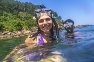 Happy couple snorkeling together in the ocean near the rocky coastline, enjoying their summer