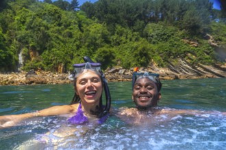 Interracial couple enjoying snorkeling in beautiful turquoise water with lush vegetation on the