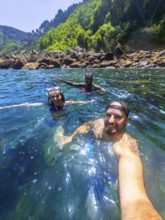 Three friends wearing snorkeling gear and enjoying the refreshing ocean water near a rocky coast