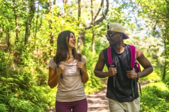 Young multi ethnic couple enjoying a hike together, walking and talking on a sunny trail in a lush