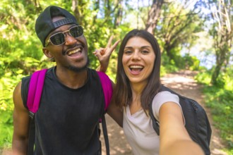 Interracial couple taking a selfie while hiking on a forest trail, enjoying their outdoor adventure