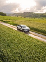 A car drives on a dirt track through a rape field under a cloudy sky, Deer E- CarSharing, Renault