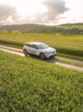 A car drives on a country lane through wide green meadows under a cloudy sky, Deer E- CarSharing,